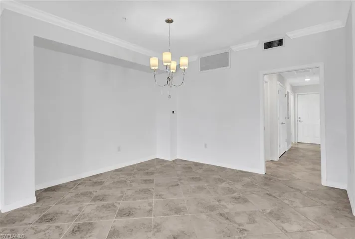 Tiled empty room featuring a notable chandelier and crown molding