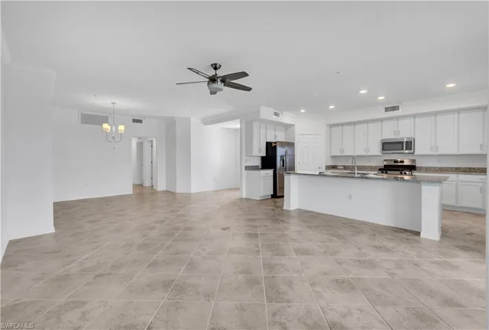 Kitchen with an island with sink, ceiling fan with notable chandelier, light tile flooring, and appliances with stainless steel finishes