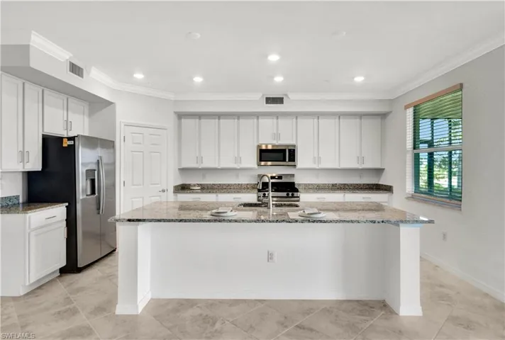 Kitchen with stainless steel appliances, dark stone counters, an island with sink, and light tile flooring