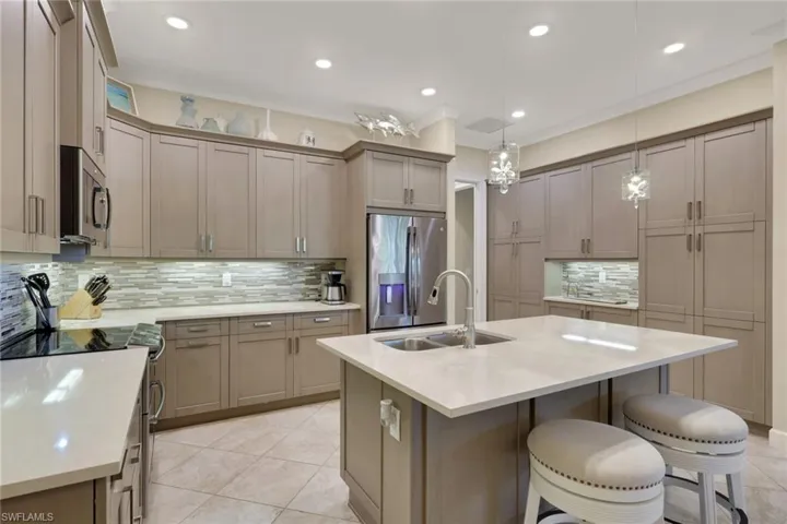 Kitchen with stainless steel appliances, a kitchen bar, a kitchen island with sink, pendant lighting, and light stone counters