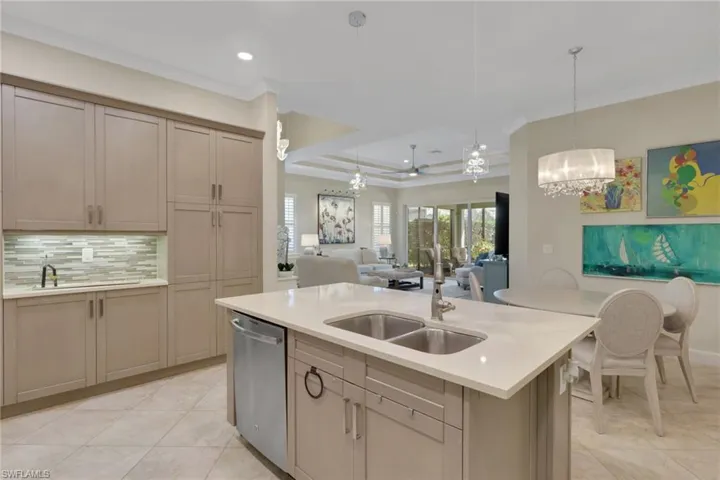 Kitchen featuring ornamental molding, open floor plan, a kitchen island with sink, a tray ceiling, and stainless steel dishwasher