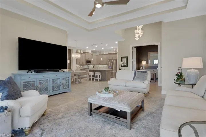 Living area with ceiling fan, ornamental molding, light tile patterned flooring, a chandelier, and a tray ceiling