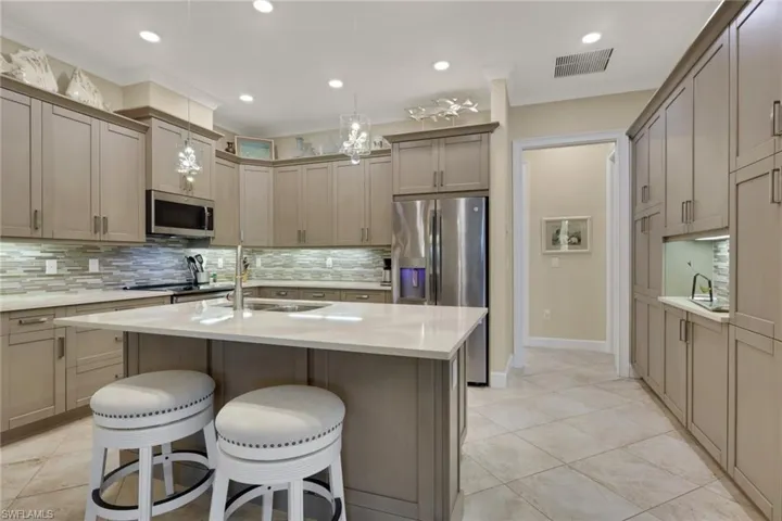 Kitchen featuring a kitchen island with sink, a breakfast bar area, light stone counters, stainless steel appliances, and backsplash