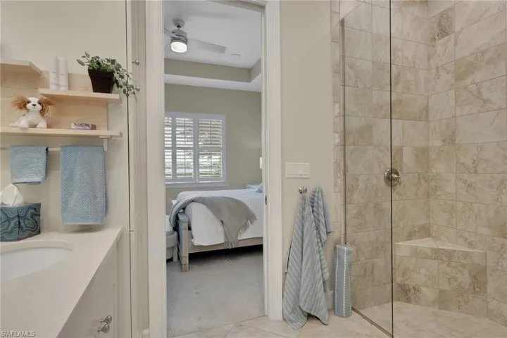 Bathroom featuring connected bathroom, vanity, a walk in shower, light colored carpet, and a ceiling fan
