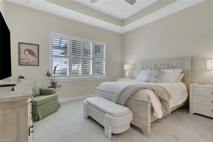 Bedroom with light carpet, ceiling fan, and a raised ceiling