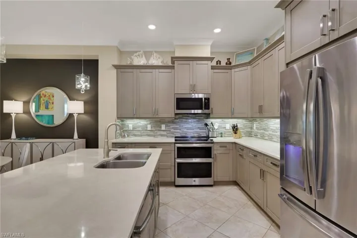 Kitchen featuring stainless steel appliances, light stone counters, decorative light fixtures, decorative backsplash, and light tile patterned floors