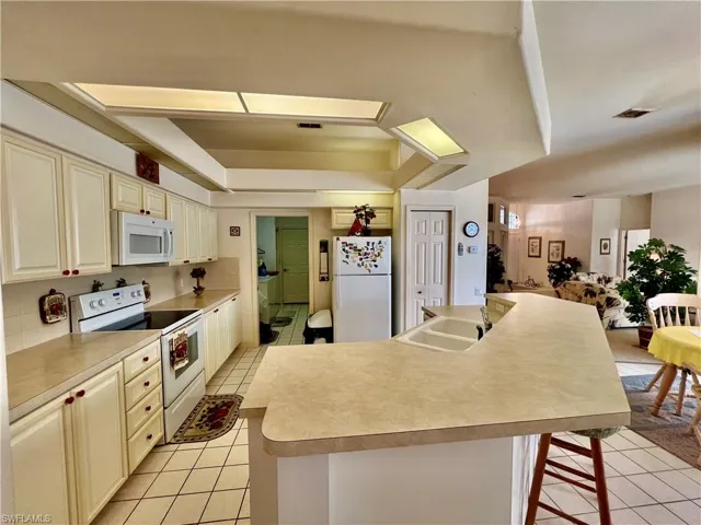 Kitchen with white appliances, tasteful backsplash, a tray ceiling, a sink, and light tile patterned flooring