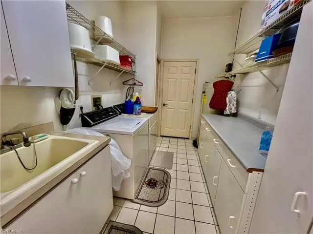 Washroom featuring light tile patterned floors, a sink, washing machine and dryer, and cabinet space