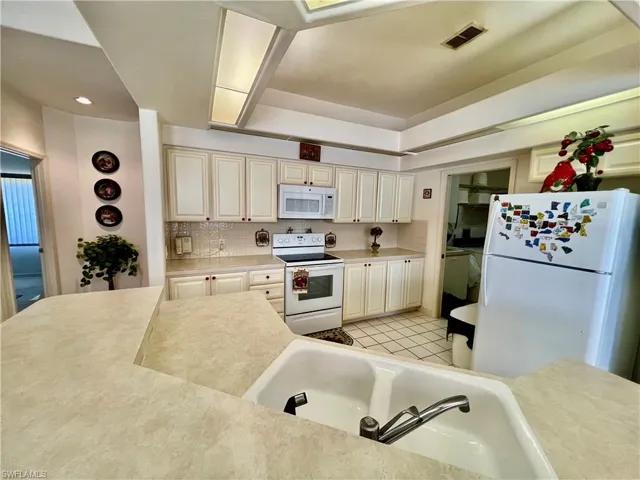 Kitchen with light tile patterned floors, light countertops, visible vents, backsplash, and white appliances