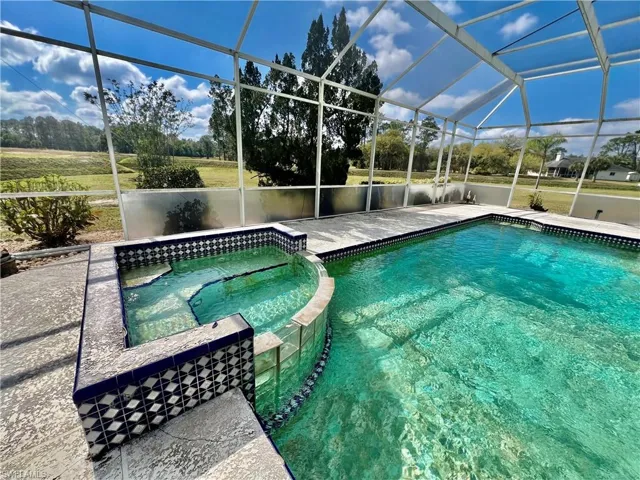 Pool with screen enclosure, a patio, and an in ground hot tub