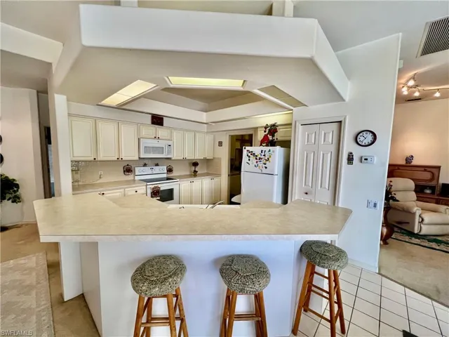 Kitchen with light tile patterned flooring, white appliances, a breakfast bar, visible vents, and cream cabinetry