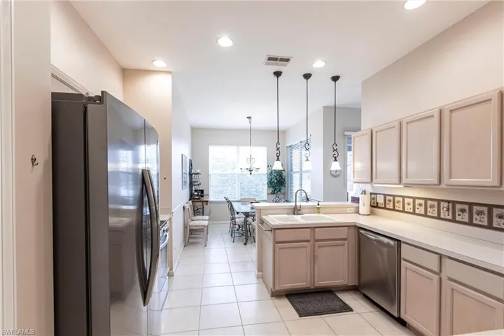 Kitchen with light brown cabinetry, sink, hanging light fixtures, kitchen peninsula, and stainless steel appliances