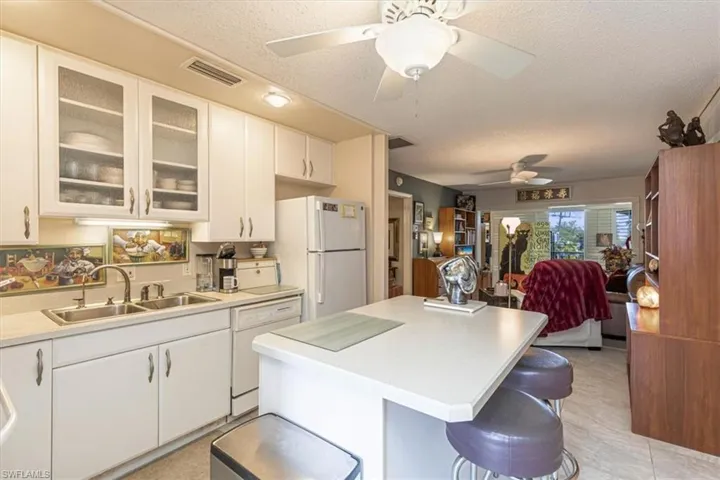 Kitchen with glass fronted cabinets, a kitchen island, light countertops, white cabinetry, and a kitchen breakfast bar