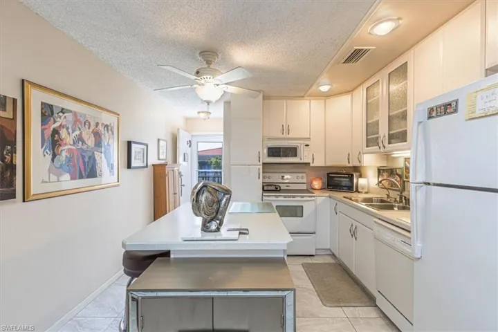 Kitchen featuring glass fronted cabinets, white appliances, light countertops, a kitchen island, and ceiling fan