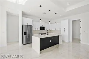 Kitchen featuring a center island with sink, stainless steel fridge with ice dispenser, and white cabinetry