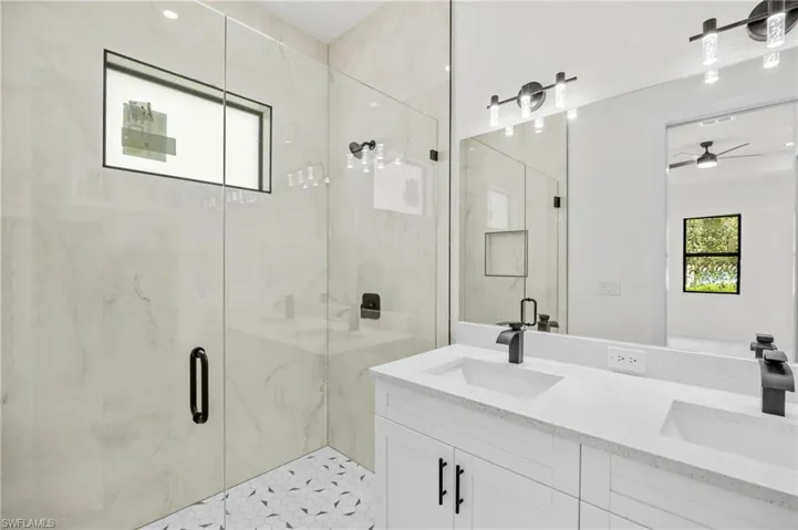 Full bathroom with double vanity, a marble finish shower, and ceiling fan
