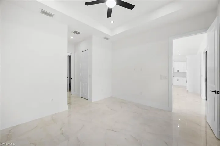 Empty room featuring recessed lighting, a raised ceiling, light marble finish flooring, and ceiling fan