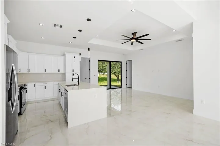 Kitchen featuring white cabinets, an island with sink, light stone counters, hanging light fixtures, and stainless steel appliances