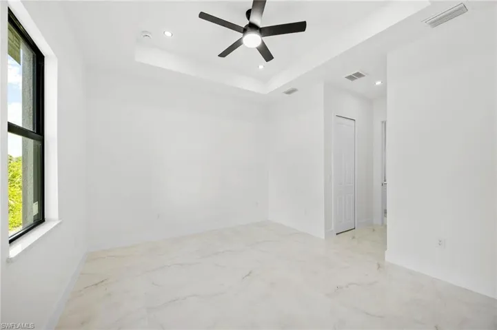 Spare room featuring a tray ceiling, light marble finish flooring, a ceiling fan, and recessed lighting