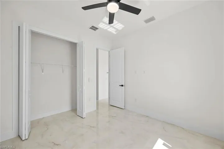 Unfurnished bedroom featuring light marble finish floors, a ceiling fan, and a closet