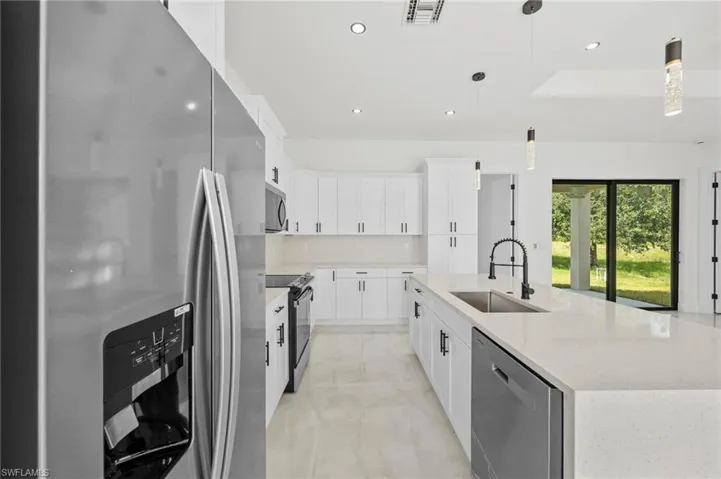 Kitchen featuring stainless steel appliances, a spacious island, white cabinets, light stone countertops, and pendant lighting