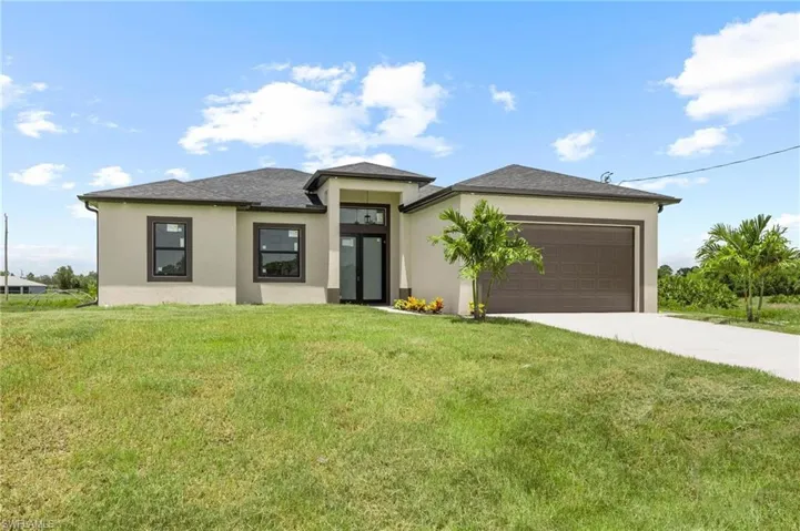 Prairie-style home featuring a front lawn, concrete driveway, a garage, stucco siding, and french doors