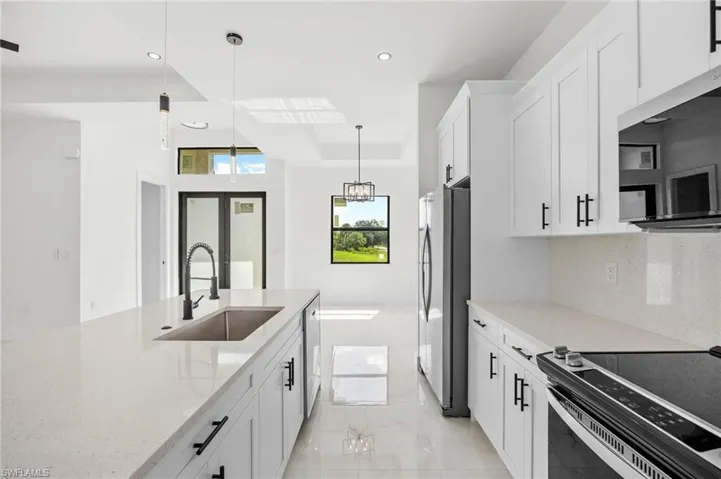 Kitchen with white cabinets, stainless steel appliances, light stone counters, and hanging light fixtures