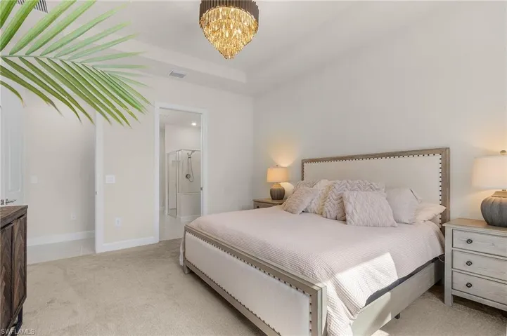 Bedroom with light colored carpet, a chandelier, and ensuite bath