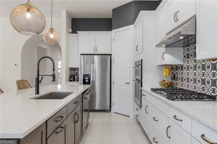 Kitchen featuring appliances with stainless steel finishes, a sink, under cabinet range hood, arched walkways, and backsplash