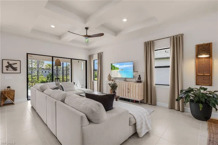 Living room featuring coffered ceiling, light tile patterned flooring, beam ceiling, and a ceiling fan