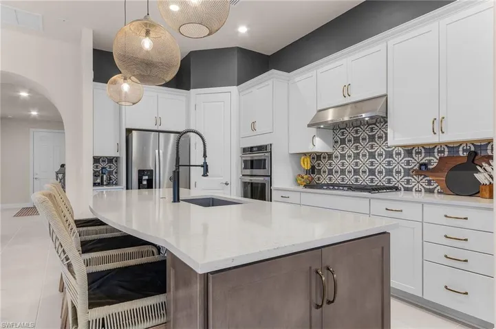 Kitchen featuring under cabinet range hood, stainless steel appliances, tasteful backsplash, arched walkways, and a kitchen island with sink