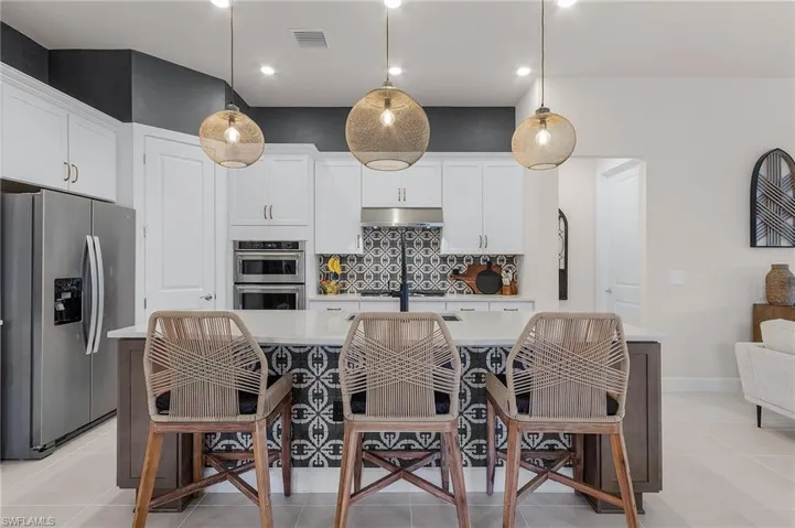 Kitchen with appliances with stainless steel finishes, under cabinet range hood, light countertops, decorative backsplash, and white cabinetry