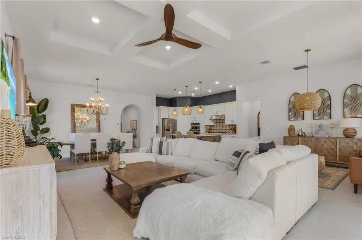 Living room featuring light tile patterned floors, arched walkways, coffered ceiling, a ceiling fan, and a chandelier