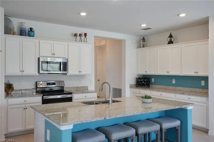 Kitchen featuring a center island with sink, stainless steel appliances, open floor plan, and white cabinetry