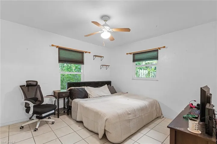 Tiled bedroom featuring ceiling fan and multiple windows