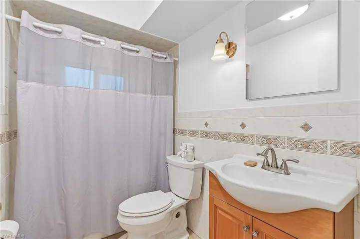Bathroom with tile walls, walk in shower, vanity, and toilet