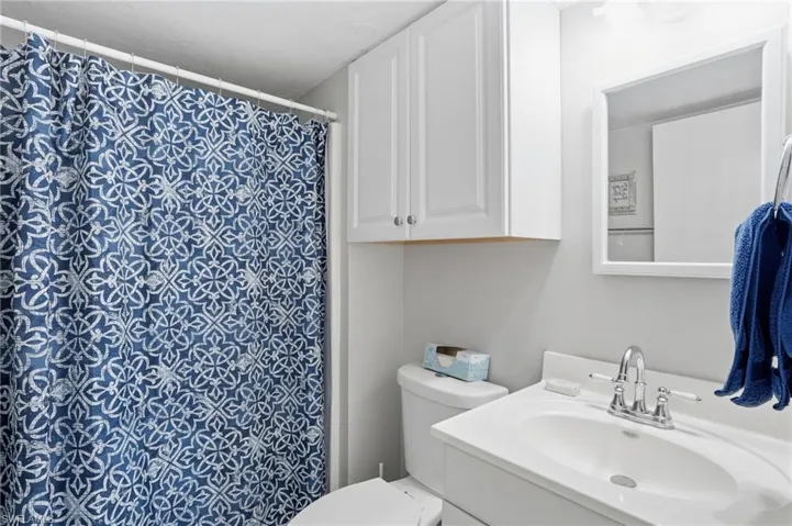 Primary Bathroom featuring a white vanity with integrated sink, chrome faucet, wall-mounted mirror, and white overhead cabinetry - Virtually Edited Image