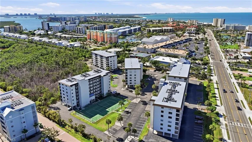 Aerial perspective showcasing multiple residential buildings, a tennis court, and parking areas - Virtually Edited Image