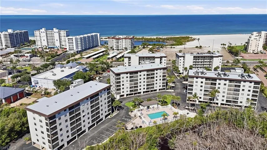 Aerial view of multiple multi-story residential buildings featuring balconies, a swimming pool with surrounding patio, and palm trees - Virtually Edited Image