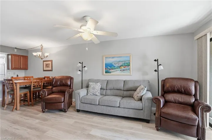 Open-concept living space featuring wood-finish flooring, a ceiling fan with integrated lighting, and light gray wall paint - Virtually Edited Image