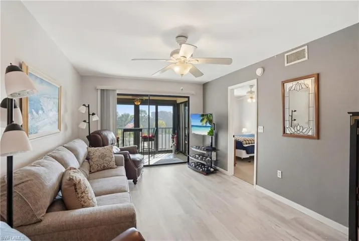 Spacious living area featuring light wood-finish flooring, a ceiling fan, and access to an outdoor balcony through sliding glass doors - Virtually Edited Image