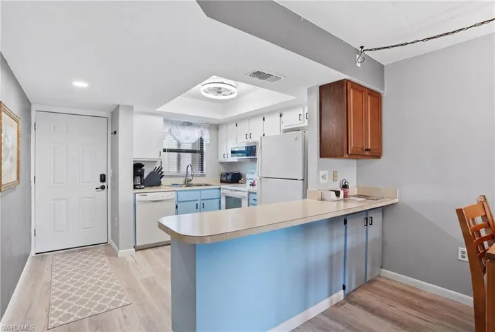 Kitchen featuring light wood-finish flooring, white appliances, and a breakfast bar - Virtually Edited Image