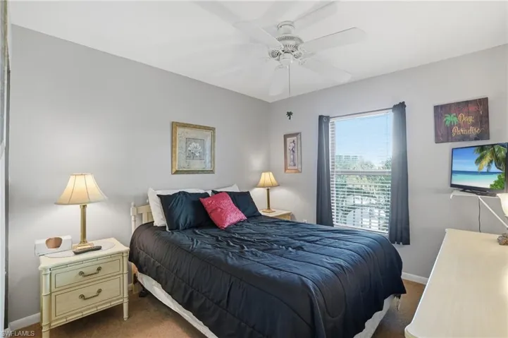 Bedroom featuring a ceiling fan, wall-mounted television, and a window with blinds and dark curtains - Virtually Edited Image
