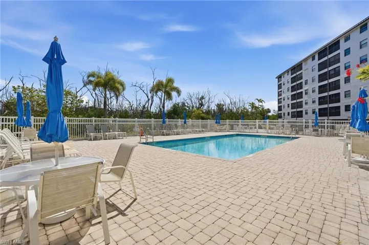 Outdoor swimming pool surrounded by a paver deck, white perimeter fencing, and established palm trees - Virtually Edited Image