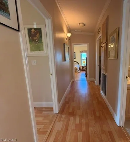 Hallway featuring wood-finish flooring, crown molding, and built-in cabinetry