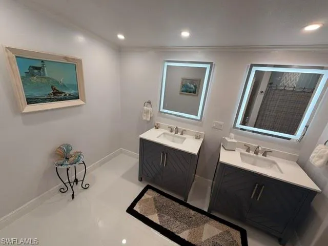 Dual vanities with chevron-patterned cabinetry, solid-surface countertops, integrated undermount sinks, and LED-backlit mirrors