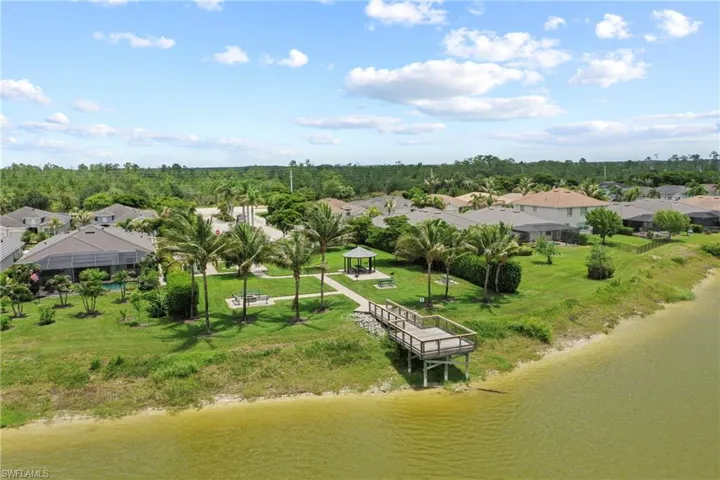 Waterfront community with a private dock, expansive green spaces, mature palm trees, and a shaded gazebo