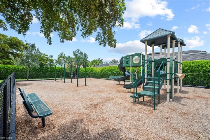 Outdoor recreational area featuring a playground structure with multiple slides and climbing elements, a swing set, and two green metal benches