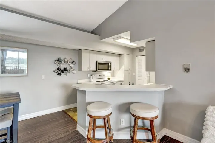 Kitchen with kitchen peninsula, dark hardwood / wood-style flooring, white cabinets, a breakfast bar, and white range with electric stovetop