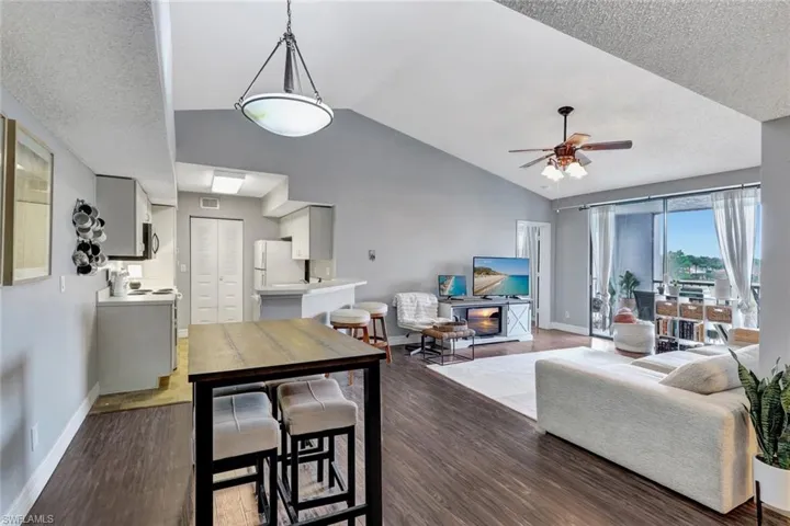 Living room with vaulted ceiling, ceiling fan, a textured ceiling, and wood-type flooring